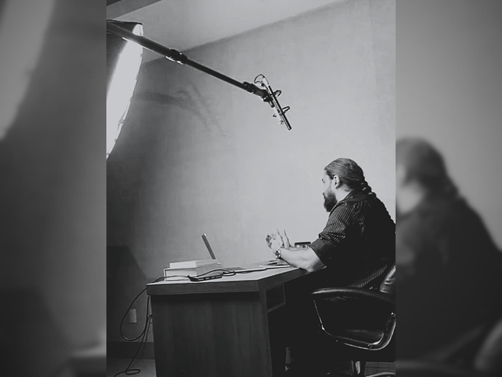 Dr. Bruno Marinho de Sousa sentado com um microfone e uma luz à esquerda, num set up de gravação de seu consultório.